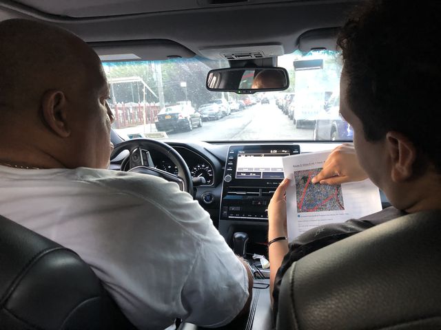 Two men sit in the driver's seat and passenger seat of a car, looking at a map.